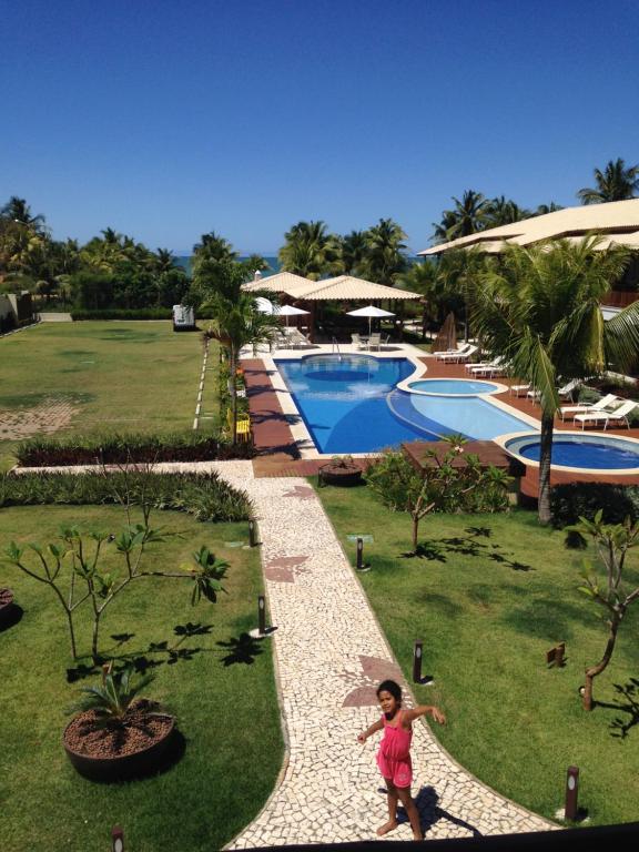 a little girl standing in front of a swimming pool at 3 Suítes, praia e piscina in Itacimirim