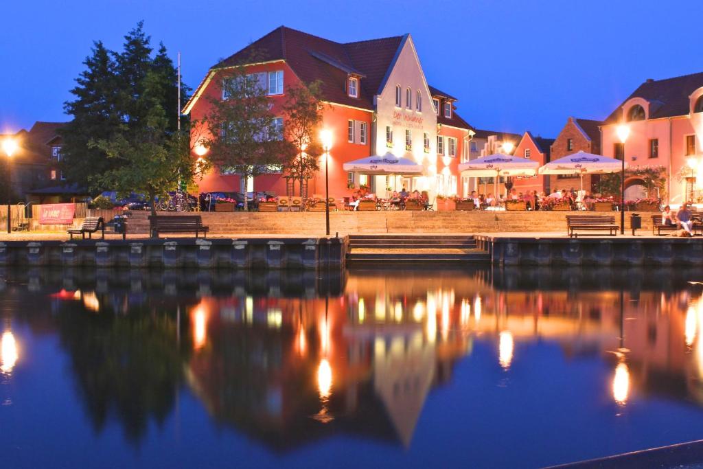 un grupo de edificios junto a un río por la noche en Der Insulaner - Hotel & Restaurant en Malchow