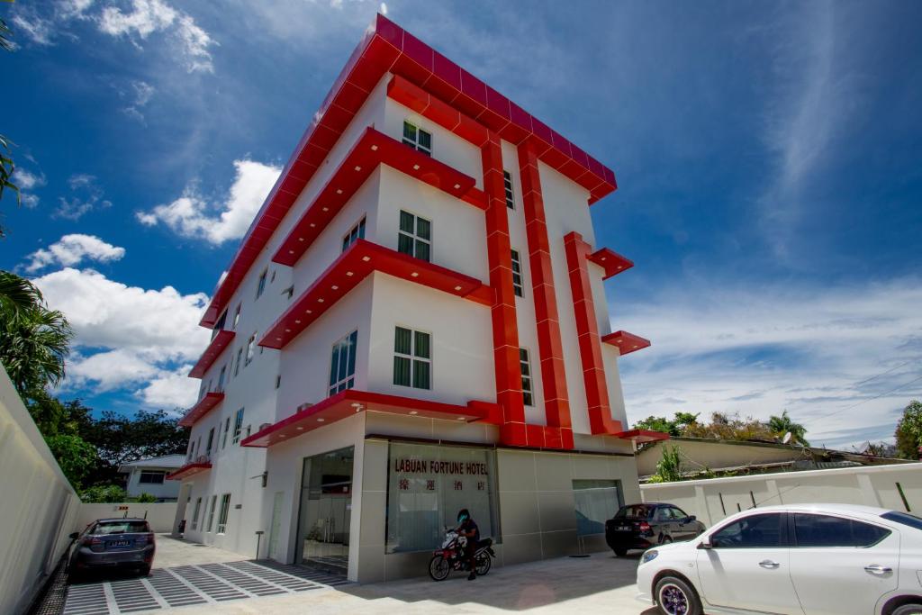 Labuan Fortune Hotel في لابوان: مبنى احمر وبيض فيه سيارات متوقفة في الامام