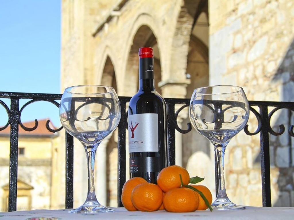 une bouteille de vin et deux verres d'oranges sur une table dans l'établissement Cefalù Cathedral Palace, à Cefalù