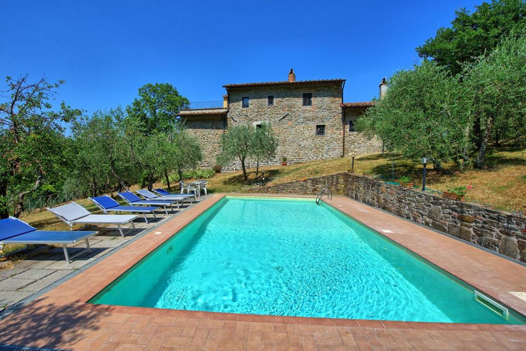 a swimming pool with chairs and a building in the background at Villa Poggio Conca by PosarelliVillas in Incisa in Valdarno