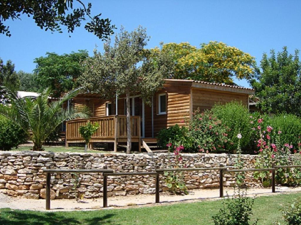 Cabaña de madera con pared de piedra y valla en Camping L'Orangeraie, en Cálig