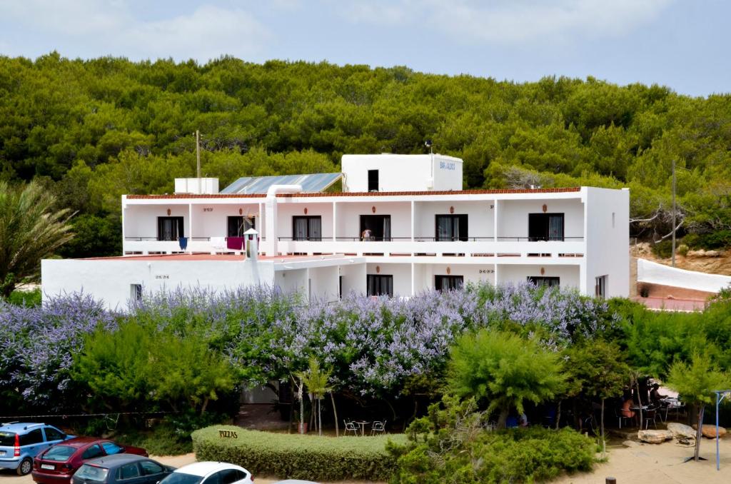 un edificio bianco con auto parcheggiate in un parcheggio di Hostal Alocs a Playa d'Es Figueral