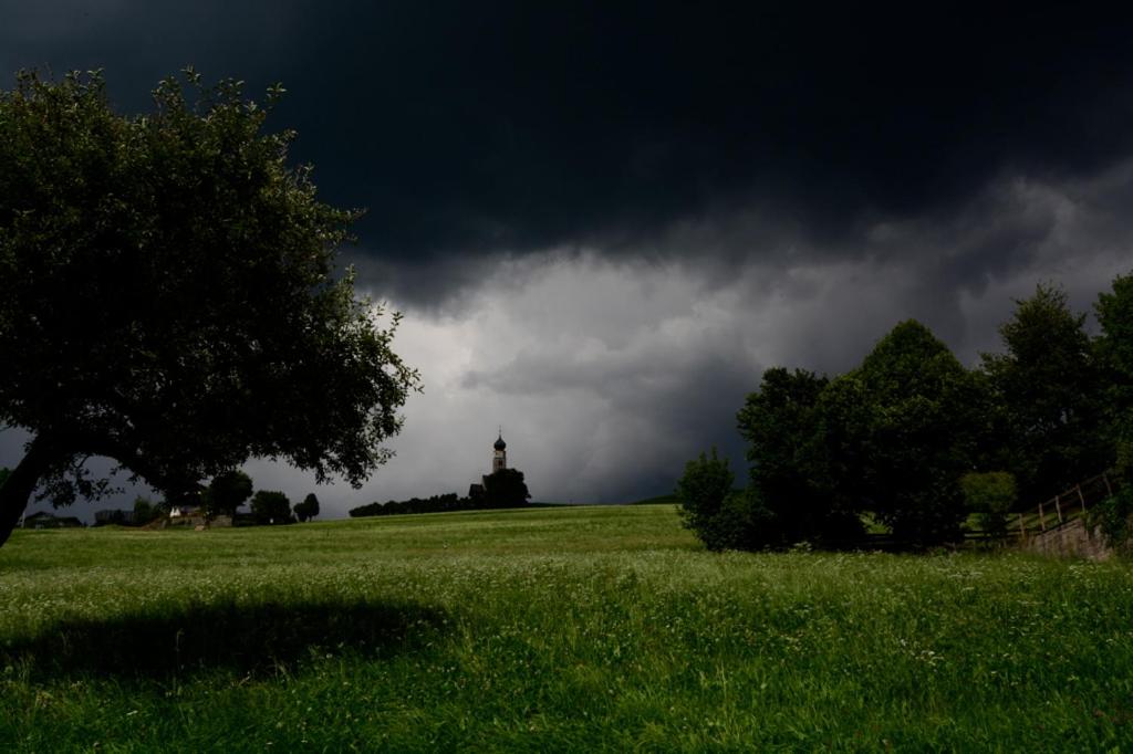 a field with a tower in the distance with a dark sky at Residence Kampidell in Siusi
