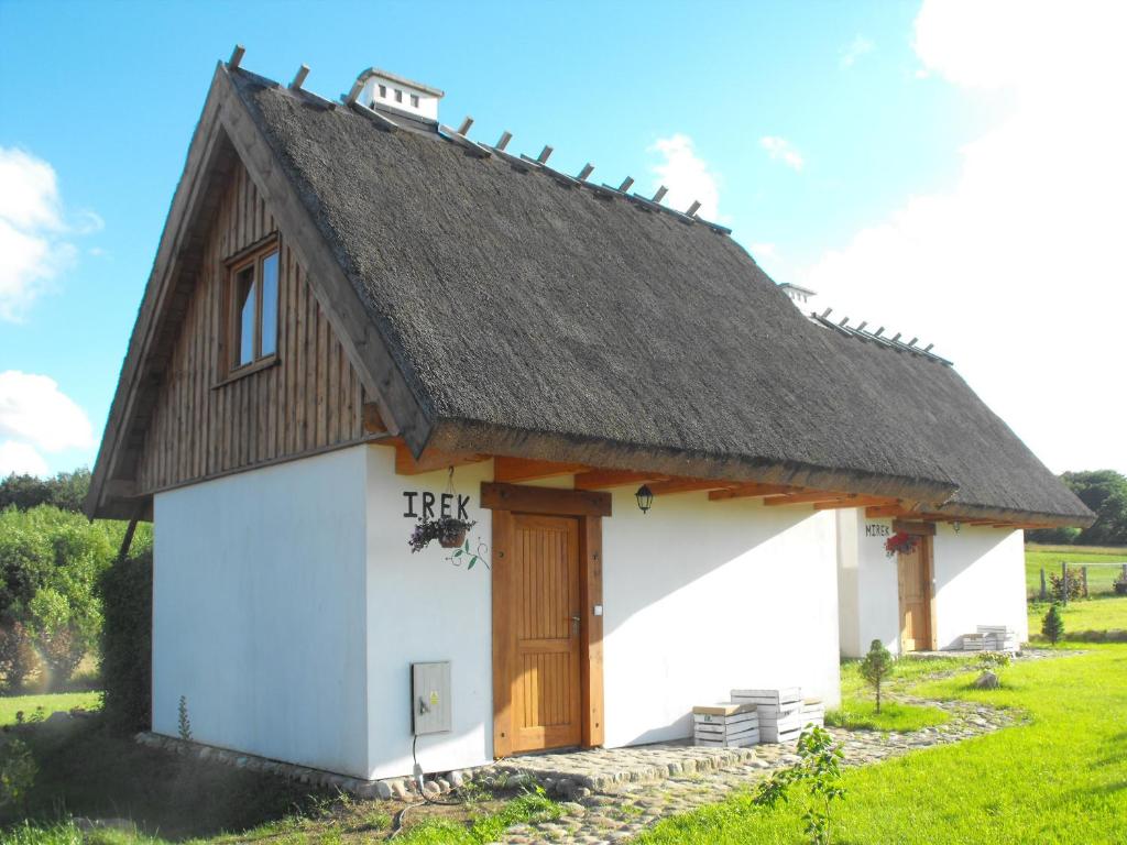 a small white building with a thatched roof at Domki przy lesie in Werblinia
