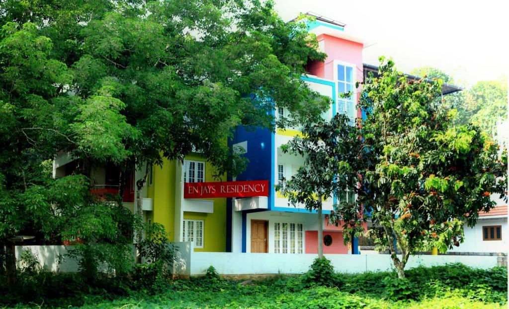 un bâtiment coloré avec des arbres devant lui dans l'établissement EN Jays Residency (Service Apartments), à Kottayam