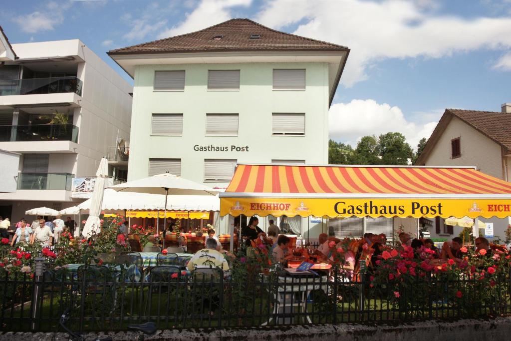 un grupo de personas sentadas en mesas frente a un edificio en Backpackers Gasthaus Post, en Willisau