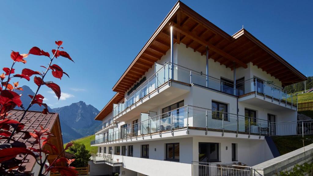 a white building with a balcony and mountains in the background at Apart Alpin in Lermoos