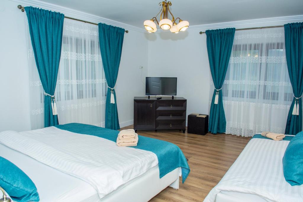 Cette chambre comprend 2 lits dans une chambre dotée de rideaux bleus et d'une télévision. dans l'établissement Casa Alin, à Haţeg