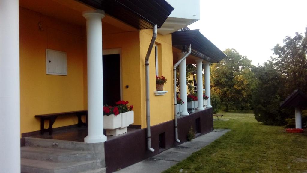 a yellow building with white columns and flowers on the porch at Júlia Vendégház in Sárospatak