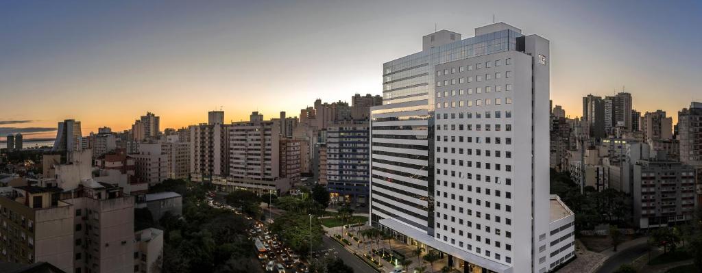 ein hohes weißes Gebäude in einer Stadt bei Sonnenuntergang in der Unterkunft Intercity Porto Alegre Cidade Baixa in Porto Alegre