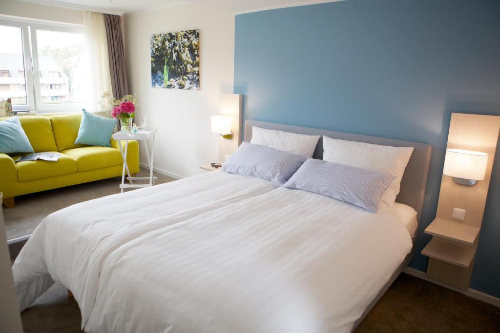 ビューズムにあるHotel Jess am Meerのベッドルーム(大きな白いベッド1台、黄色のソファ付)