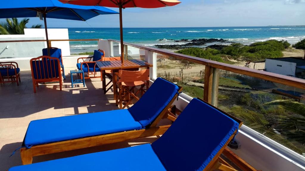 einen Balkon mit blauen Stühlen, einem Tisch und einem Sonnenschirm in der Unterkunft Drake Inn in Puerto Villamil