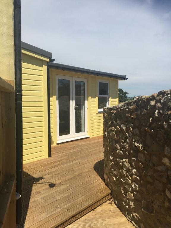 a yellow house with a wooden deck and a stone wall at The Retreat in Charmouth