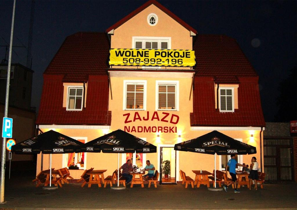 un restaurante con mesas y sombrillas frente a un edificio en Zajazd Nadmorski, en Stegna