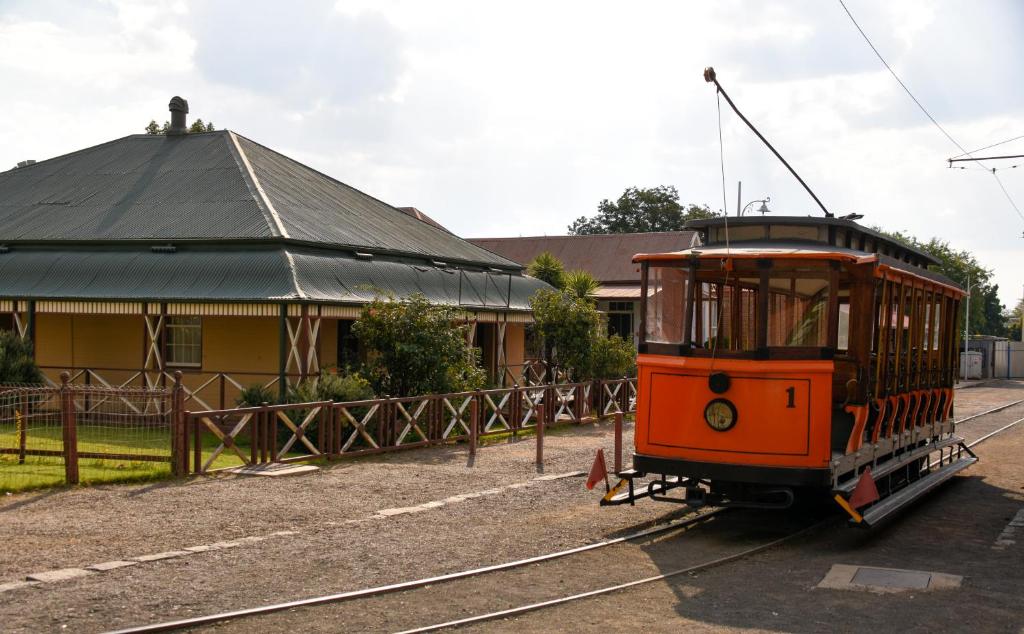 ein orangefarbener Trolleybus auf den Gleisen vor einem Gebäude in der Unterkunft New Rush Guest House in Kimberley