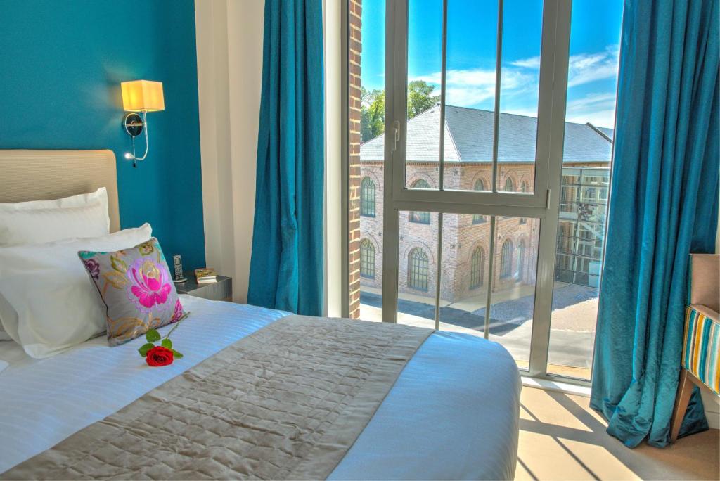 a bedroom with a bed and a large window at Hôtel de la Tabletterie in Méru