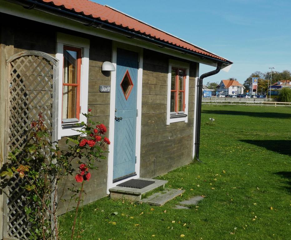 una pequeña casa con una puerta azul y una valla en Talluddens Stugby en Färjestaden