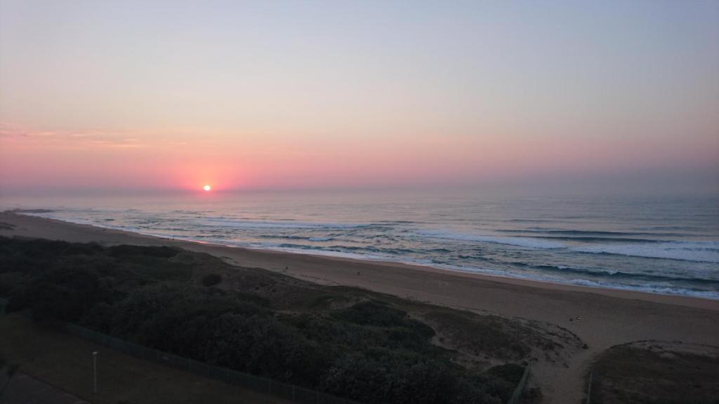 una puesta de sol sobre una playa con el océano en L'Escalier, en Amanzimtoti