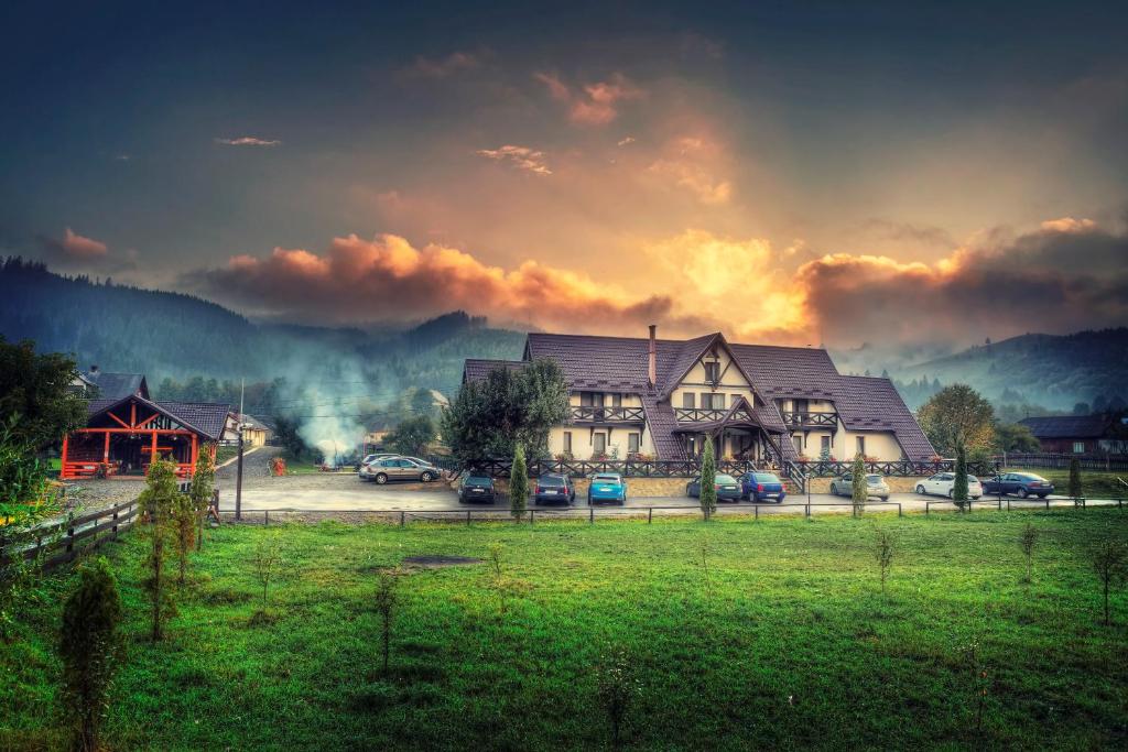 a house in a field with cars parked in front of it at La Bucovineanca in Strîmtura