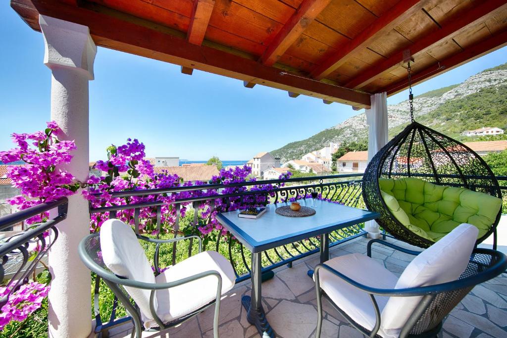 een patio met een tafel en stoelen en paarse bloemen bij Villa Kamenica in Komiža
