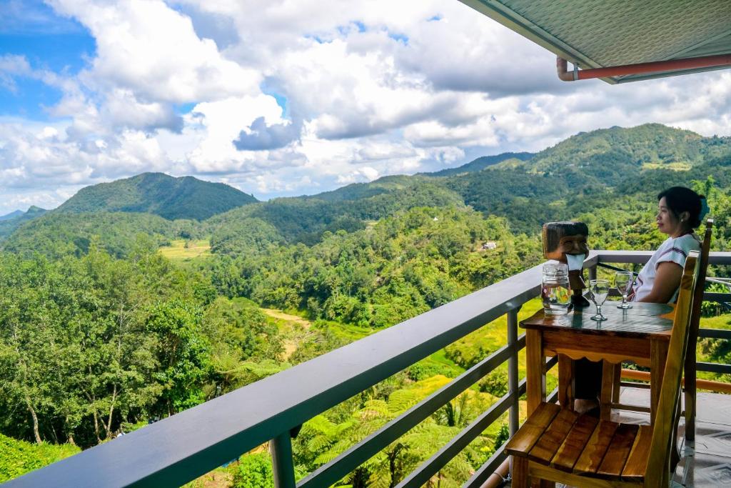 a woman sitting at a table on a balcony overlooking the mountains at Banaue Evergreen Hostel and Restaurant in Banaue