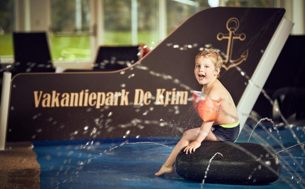 um rapaz sentado numa prancha de surf na água em Vakantiepark De Krim Texel em De Cocksdorp