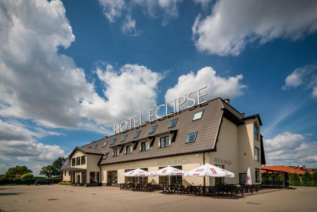 a hotel with tables and umbrellas in front of it at Hotel Eclipse in Domasław