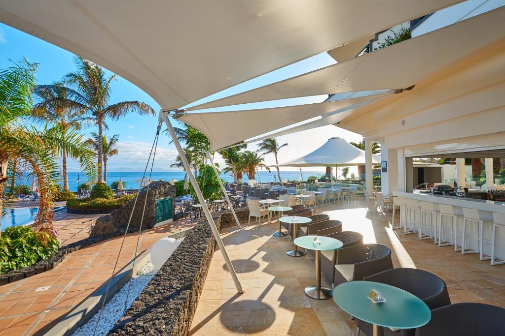 an outdoor patio with tables and chairs and the ocean at Hipotels Natura Palace Adults Only in Playa Blanca