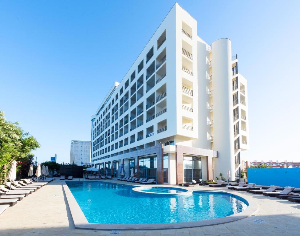 um hotel com piscina em frente a um edifício em TRYP by Wyndham Lisboa Caparica Mar em Costa da Caparica