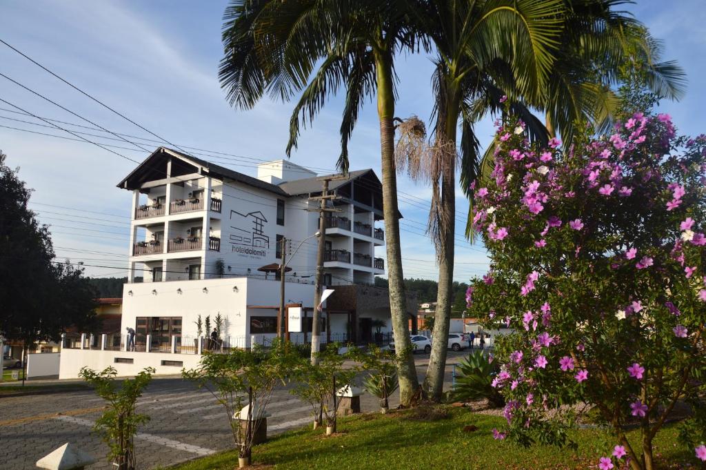 a white building with palm trees and pink flowers at Hotel Dolomiti Caravaggio in Nova Veneza