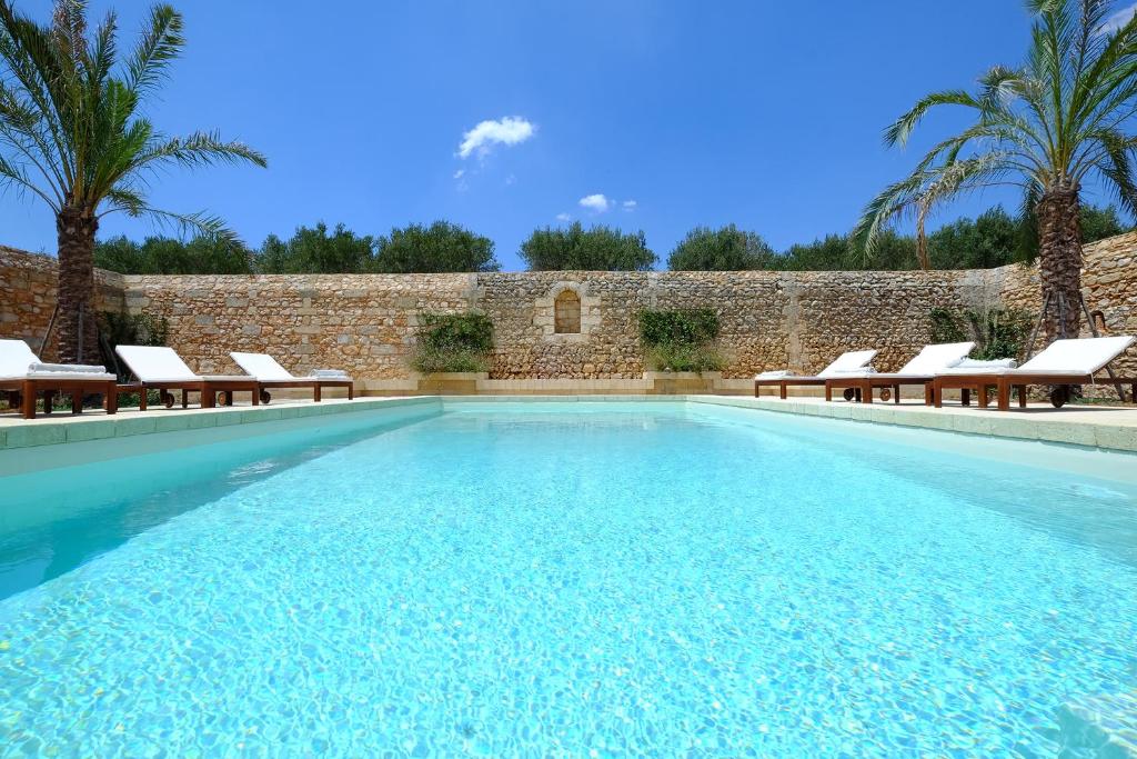 a swimming pool with chairs and a brick wall at Relais Masseria Sant'Antonio in Marina di Pescoluse