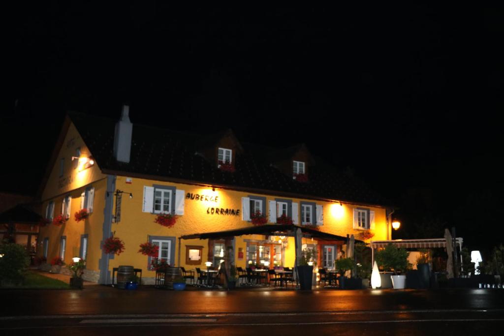 un gran edificio amarillo con mesas y sillas por la noche en Auberge Lorraine, en Le Valtin