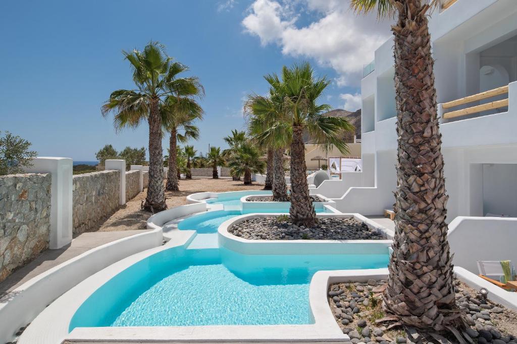 a pool with palm trees in front of a house at Casa Vitae Suites in Kamari