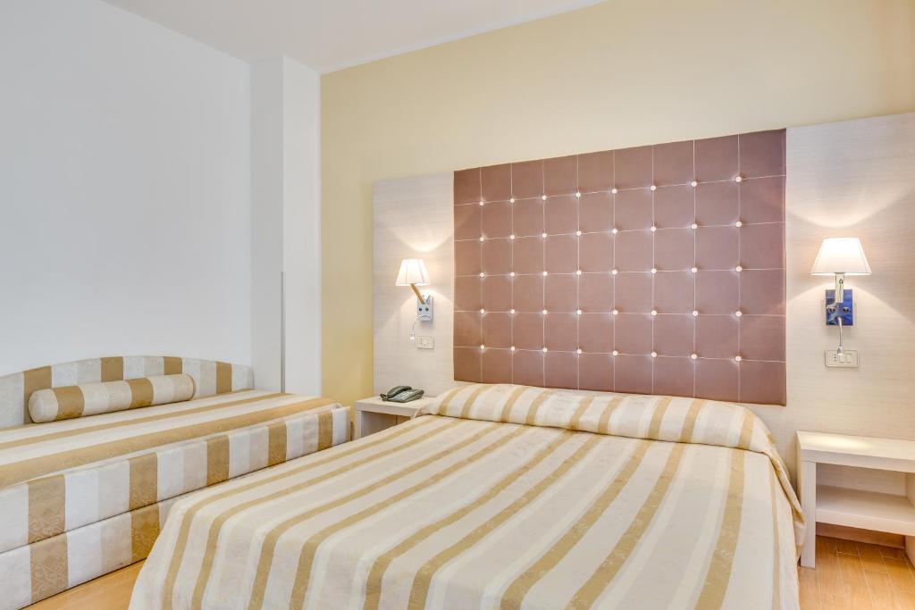 a bedroom with two beds and two lamps on the wall at Hotel Ambassador in Caorle
