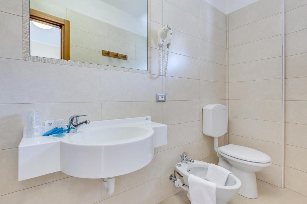 a white bathroom with a sink and a toilet at Hotel Ambassador in Caorle
