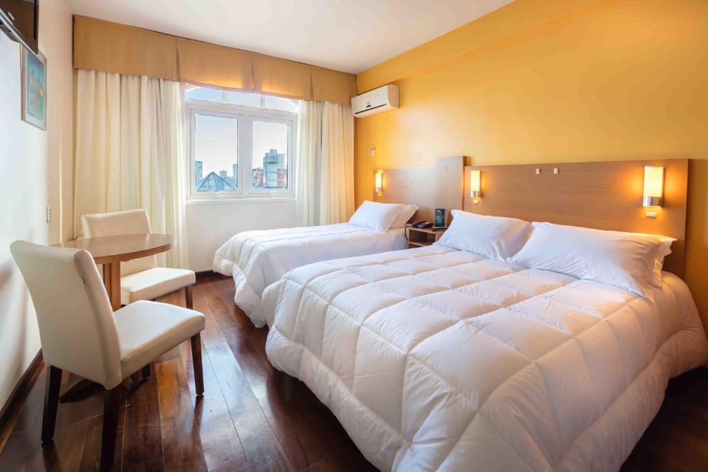 Cette chambre comprend deux lits, une table et une fenêtre. dans l'établissement San Silvestre Hotel, à Passo Fundo