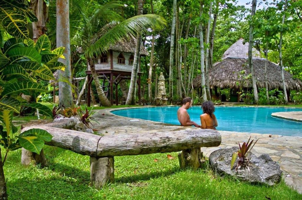 Un uomo e un ragazzo seduti su un tronco vicino a una piscina di Natura Cabana Boutique Hotel & SPA by Mint a Cabarete