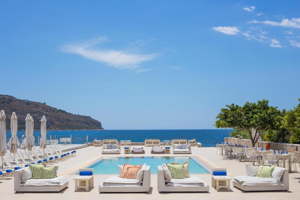 um resort com piscina e cadeiras e o oceano em Porto Vitilo Boutique Hotel em Karavostasion