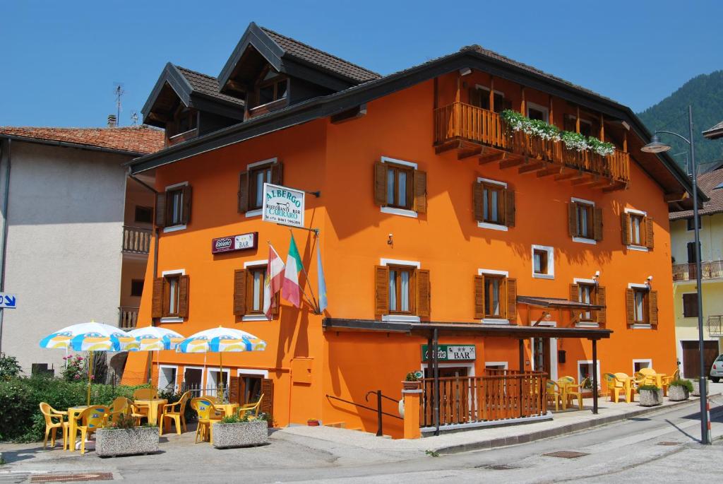 um edifício laranja com mesas e guarda-sóis em frente em Albergo Carraro em Bieno
