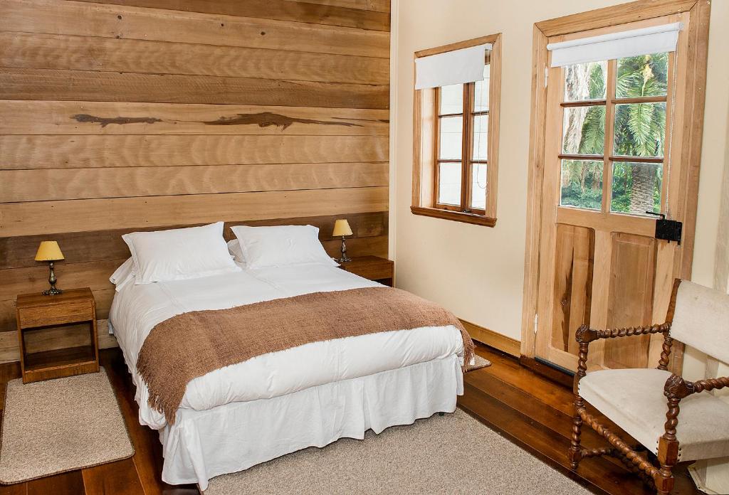 a bedroom with a bed and a chair and a window at Playa Maqui Lodge in Frutillar