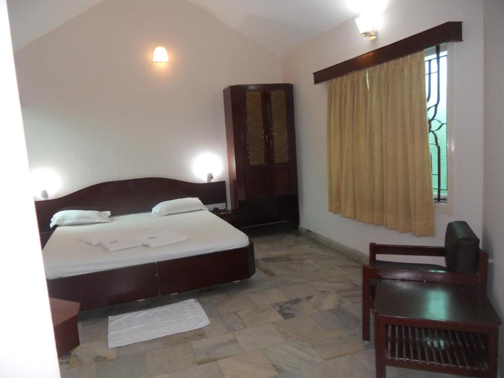 een slaapkamer met een bed, een stoel en een raam bij Hotel Sadhabishegam in Vaithīsvarankoil