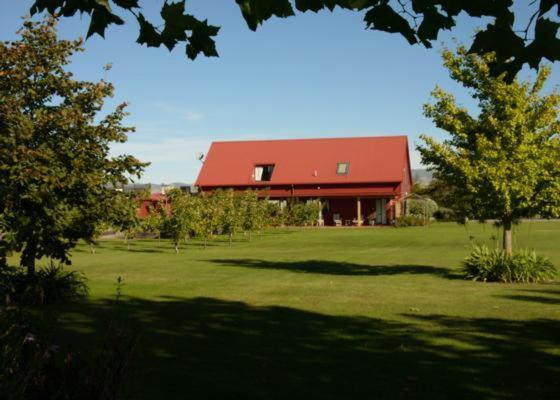 a large red building in a field with trees at Ryland Estate Guest Apartment in Kaituna