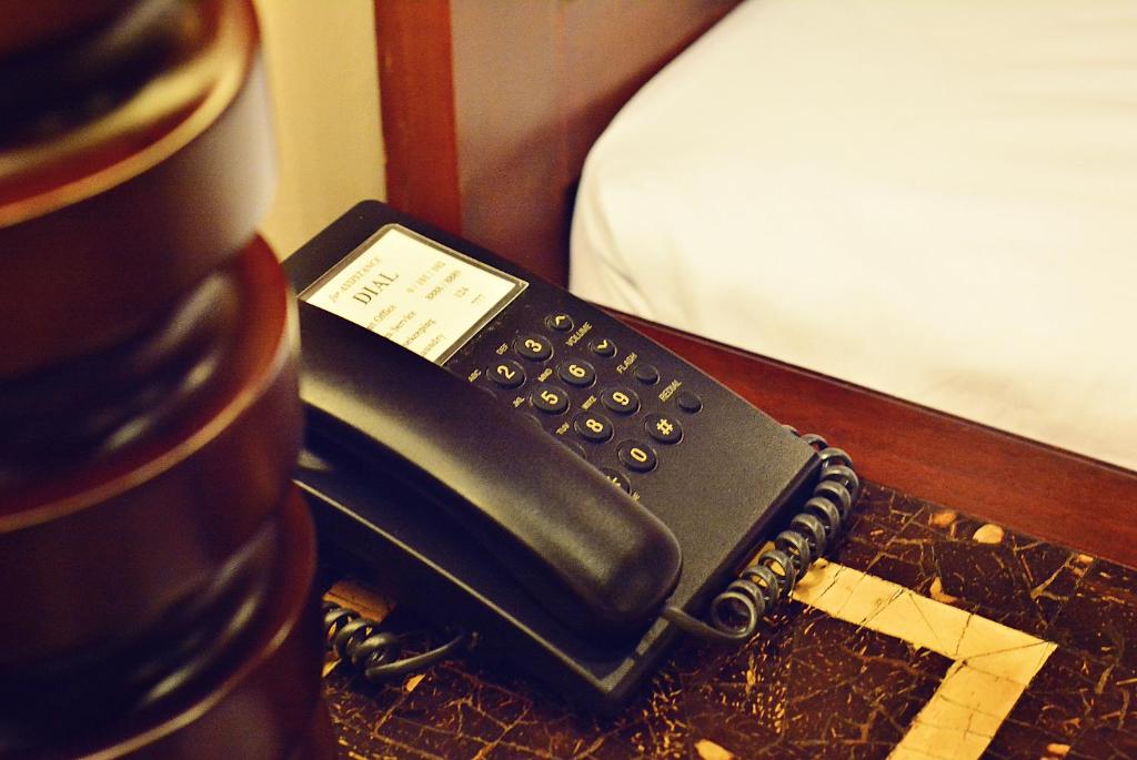 un telefono nero seduto su un tavolo accanto a un letto di Citystate Asturias Hotel Palawan a Città di Puerto Princesa