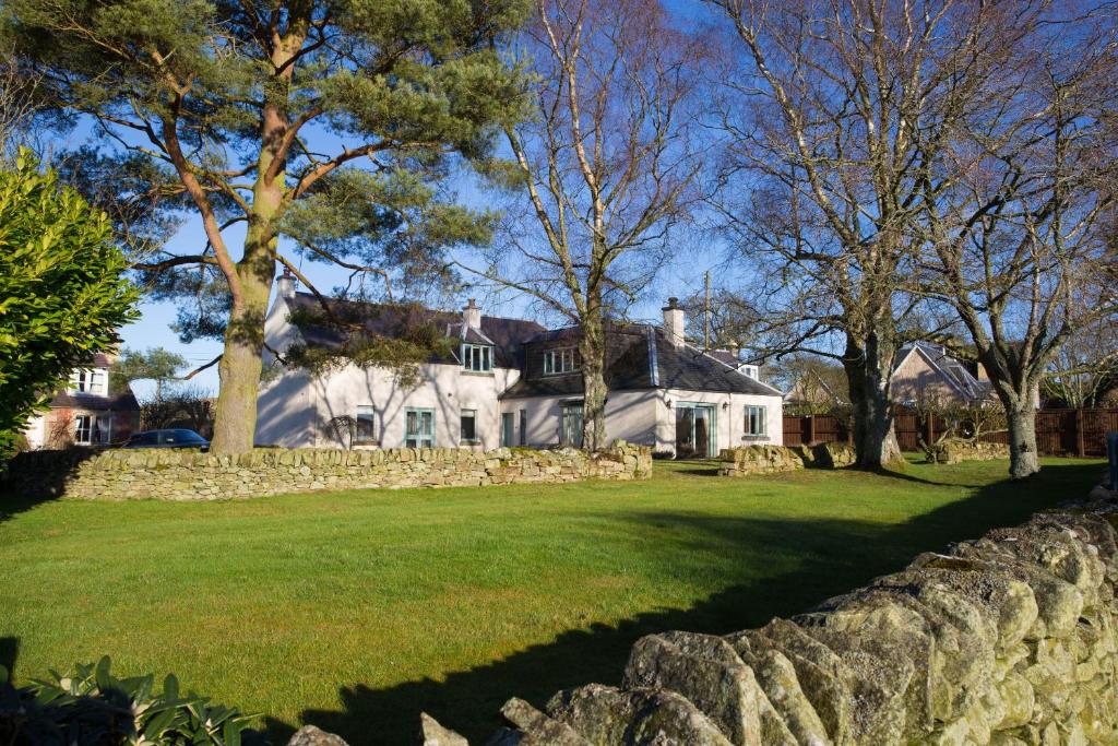una gran casa blanca con una pared de piedra y árboles en Broomfields Country House, en Melrose