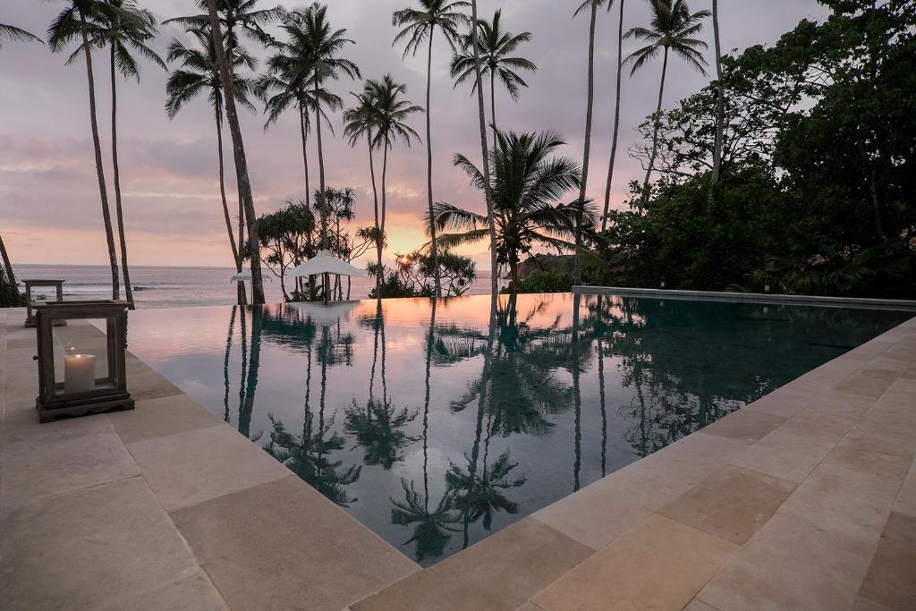 a swimming pool with a view of the ocean and palm trees at Eraeliya Villas & Gardens in Weligama