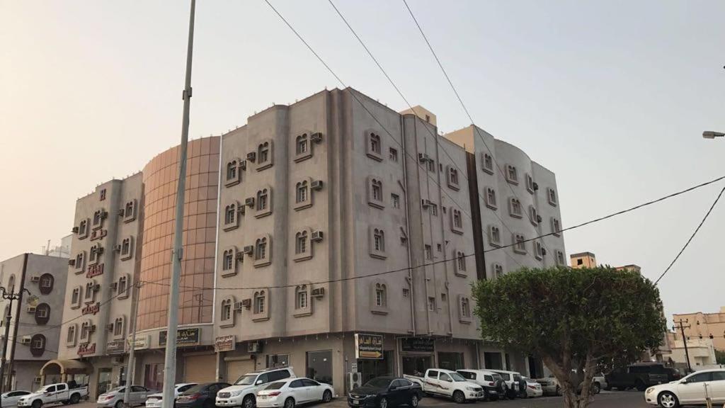 ein großes Gebäude mit Autos auf einem Parkplatz in der Unterkunft منازل الساهر للوحدات السكنية فرع 1 in Al Qunfudhah