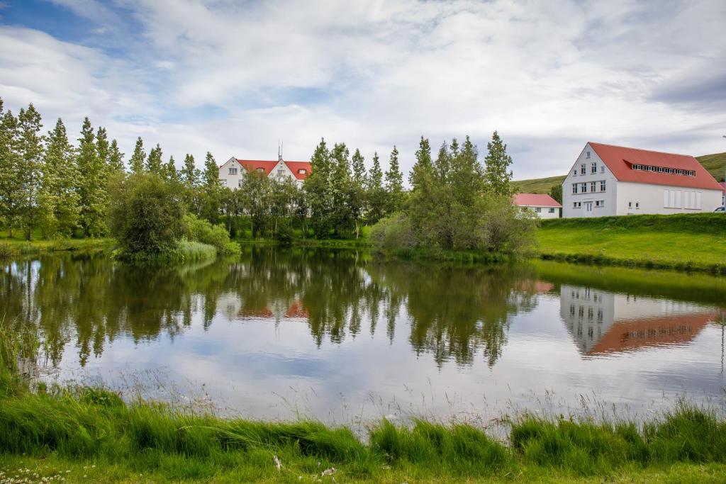 a pond with a house and a barn in the background at Hótel Laugar in Laugar