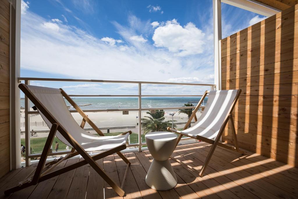 a balcony with two chairs and a view of the ocean at Hôtel Café Miramar in Le Grau-du-Roi