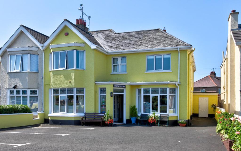 a yellow house with a bench in a parking lot at Anvershiel House in Portrush